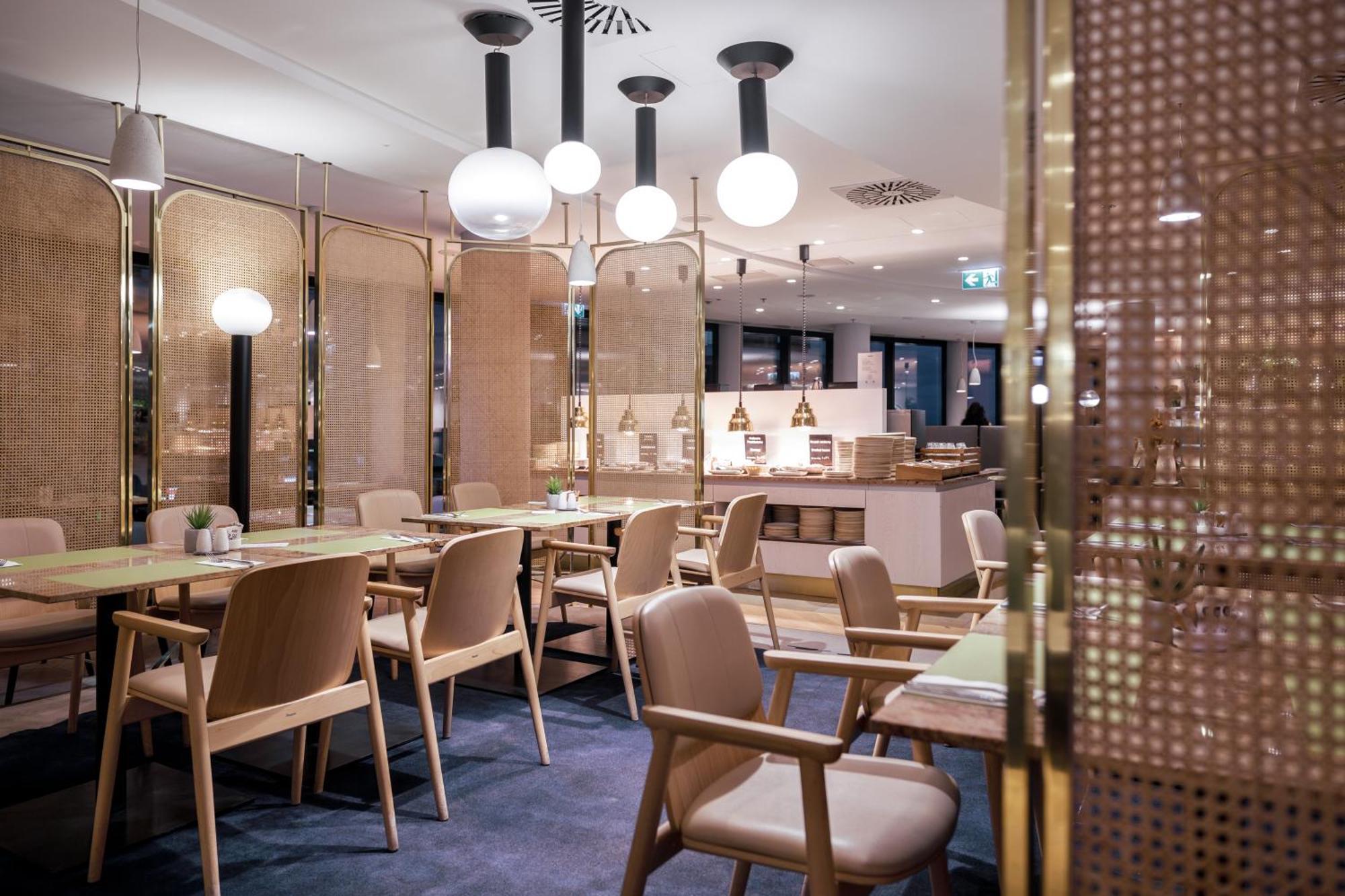 Radisson Blu Resort Świnoujście Zewnętrze zdjęcie The photo shows a modern restaurant interior. There are wooden tables and chairs arranged neatly. The atmosphere appears warm and inviting, with soft lighting provided by round pendant lamps hanging from the ceiling. Partitions made of woven material