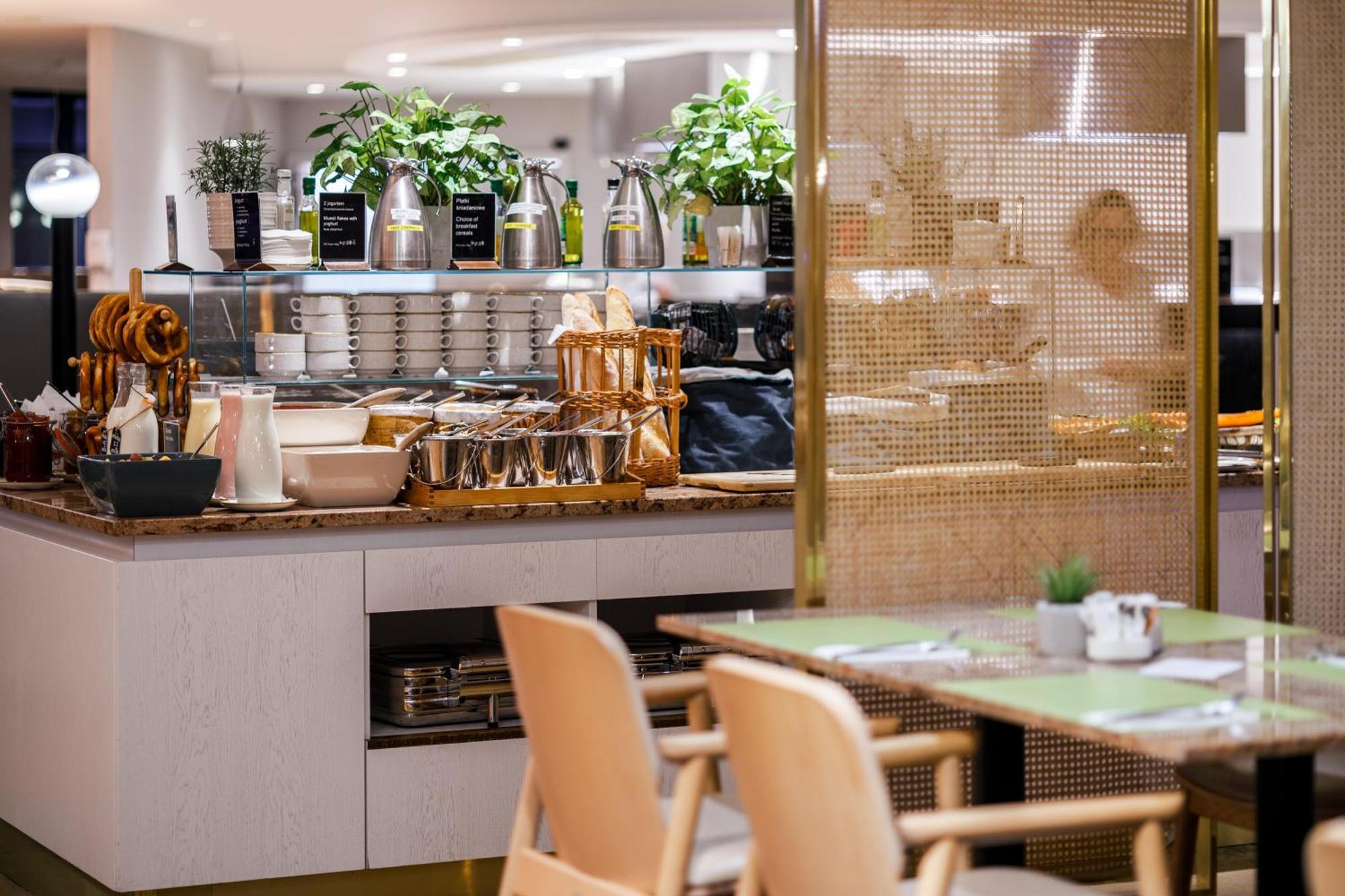 Radisson Blu Resort Świnoujście Zewnętrze zdjęcie The photo shows a modern café or dining area. In the foreground, there are wooden chairs and tables set up for dining. In the background, there is a display counter with various items, including plants in pots, containers, and possibly dishes or uten