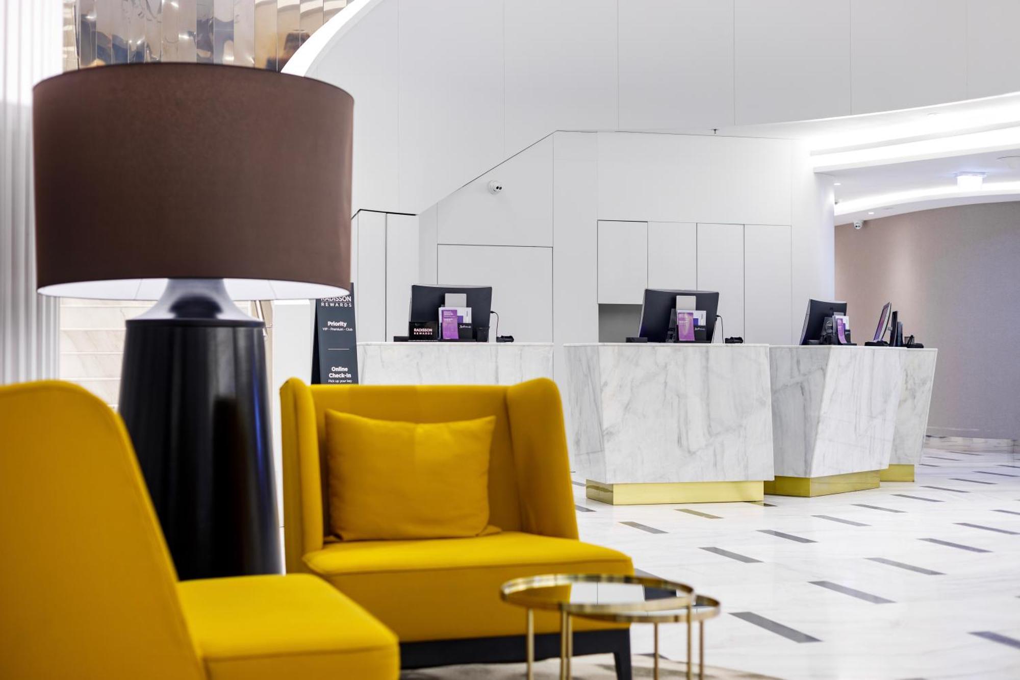 Radisson Blu Resort Świnoujście Zewnętrze zdjęcie The photo shows a modern reception area, likely of a hotel or a similar establishment. In the foreground, there are two yellow armchairs with soft cushions, situated around a small round table with a minimalist design. Behind the seating area, there 