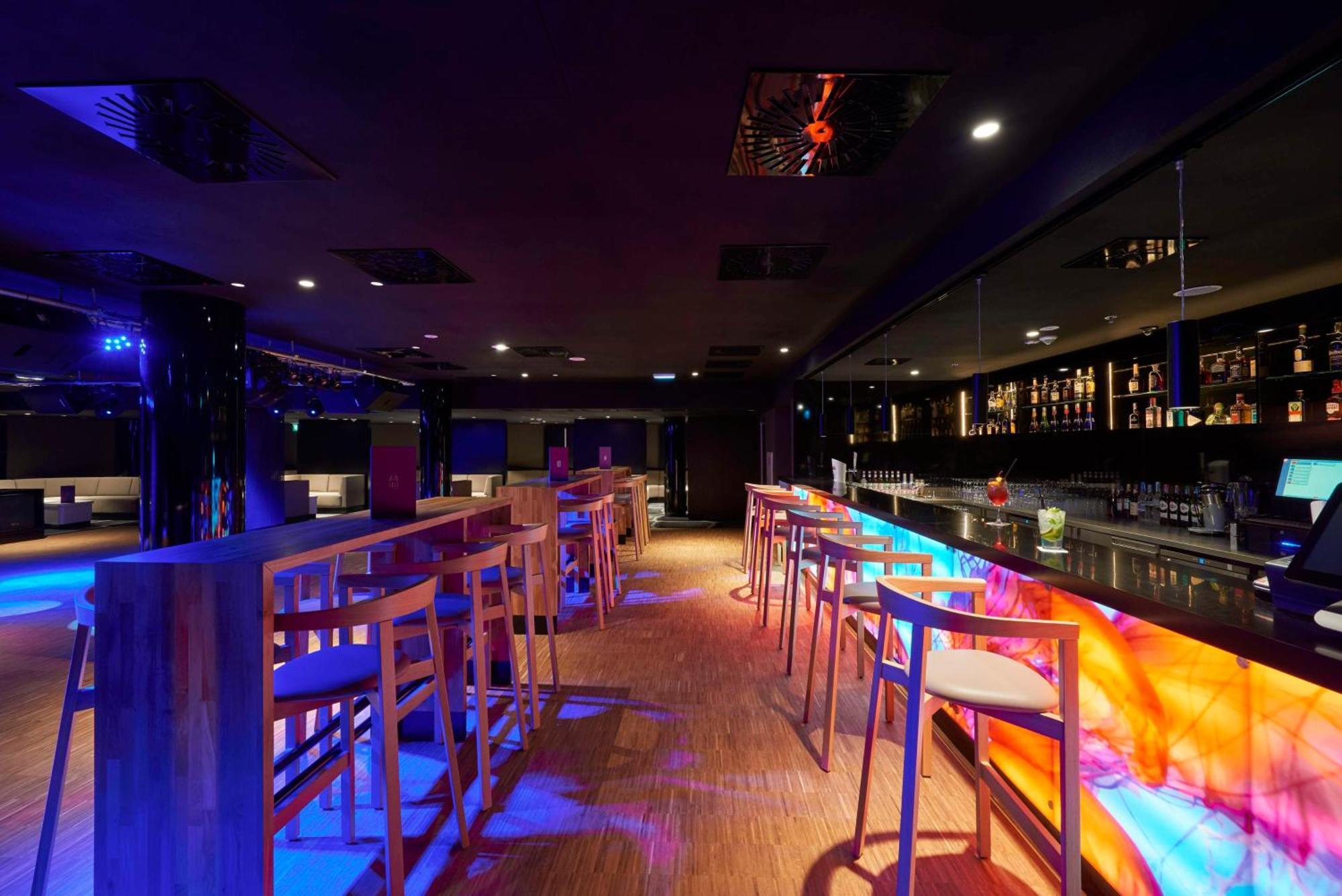 Radisson Blu Resort Świnoujście Zewnętrze zdjęcie The photo depicts a modern bar interior with a sleek and contemporary design. There are high wooden stools positioned along a bar counter, which features vibrant, colorful lighting underneath. The bar area is dimly lit, creating a nightlife ambiance,