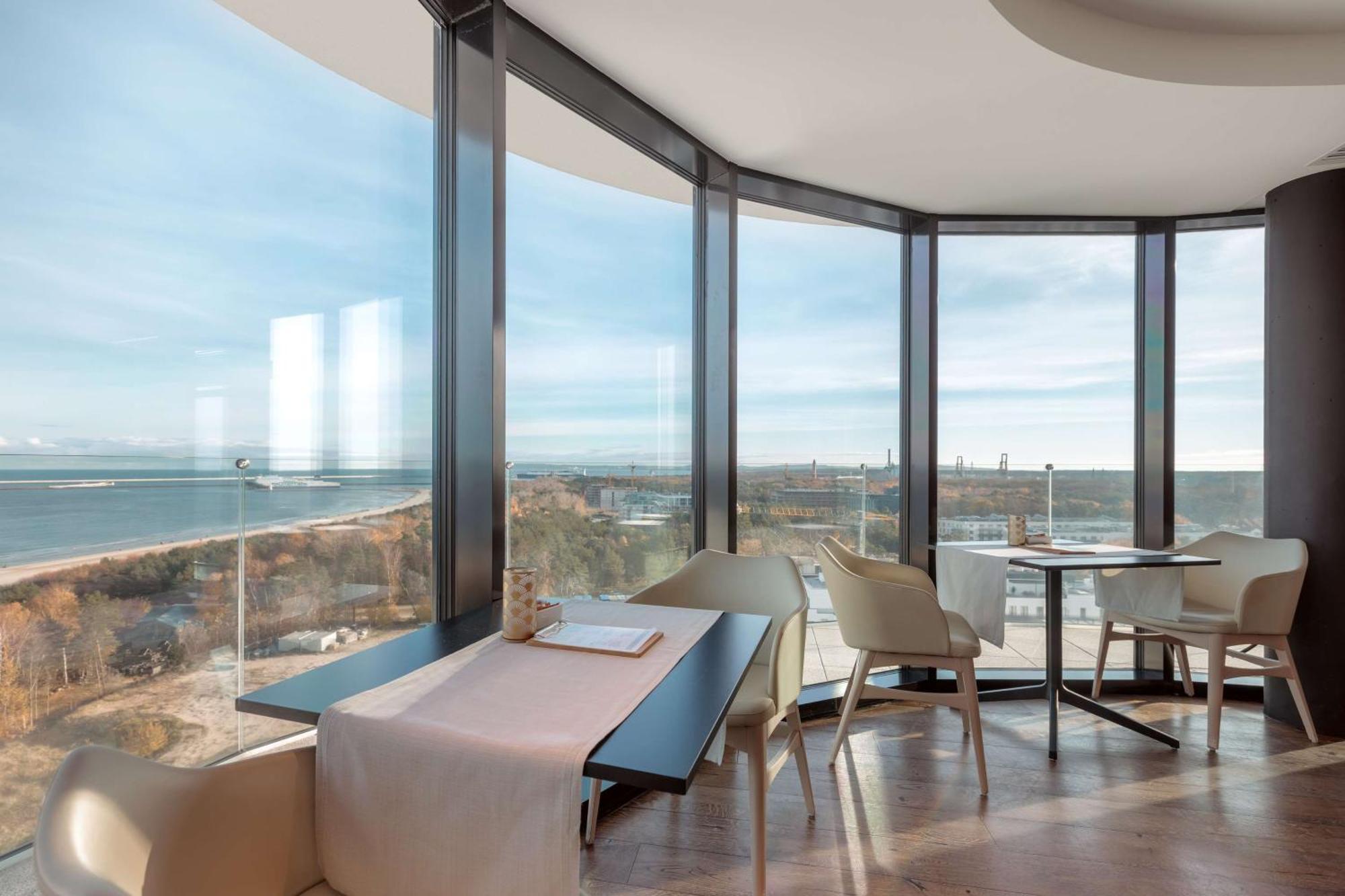 Radisson Blu Resort Świnoujście Zewnętrze zdjęcie The photo shows a modern dining area with large windows that offer a panoramic view of the landscape outside, including a body of water and possibly a shoreline. The design features sleek furniture, including a table with chairs arranged around it, a