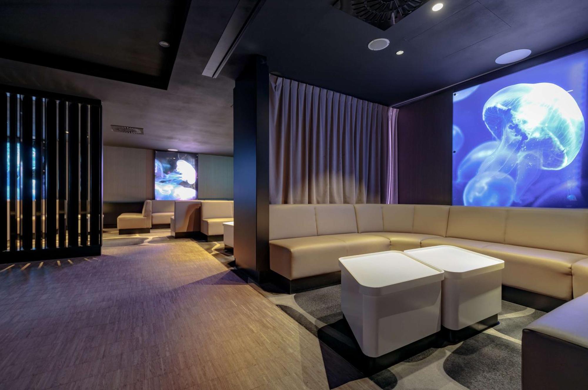 Radisson Blu Resort Świnoujście Zewnętrze zdjęcie The photo shows a modern interior space that appears to be a lounge or relaxation area. The design is sleek and minimalist, featuring a curved, light-colored seating arrangement with low tables at the center. The walls are dark, contributing to a coz