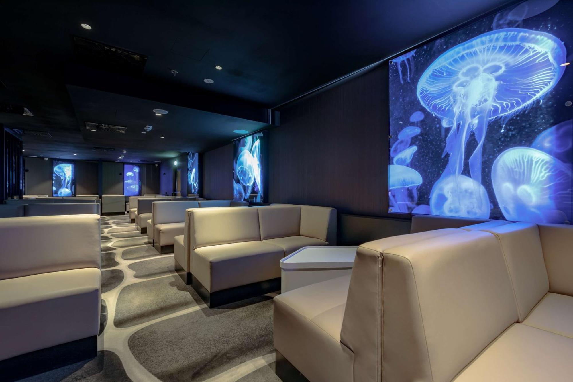 Radisson Blu Resort Świnoujście Zewnętrze zdjęcie The photo shows a modern lounge space with a sleek design. The area features light-colored, upholstered seating arranged in an open layout. The walls are decorated with large, vibrant images of jellyfish illuminated in blue, creating a calming underw