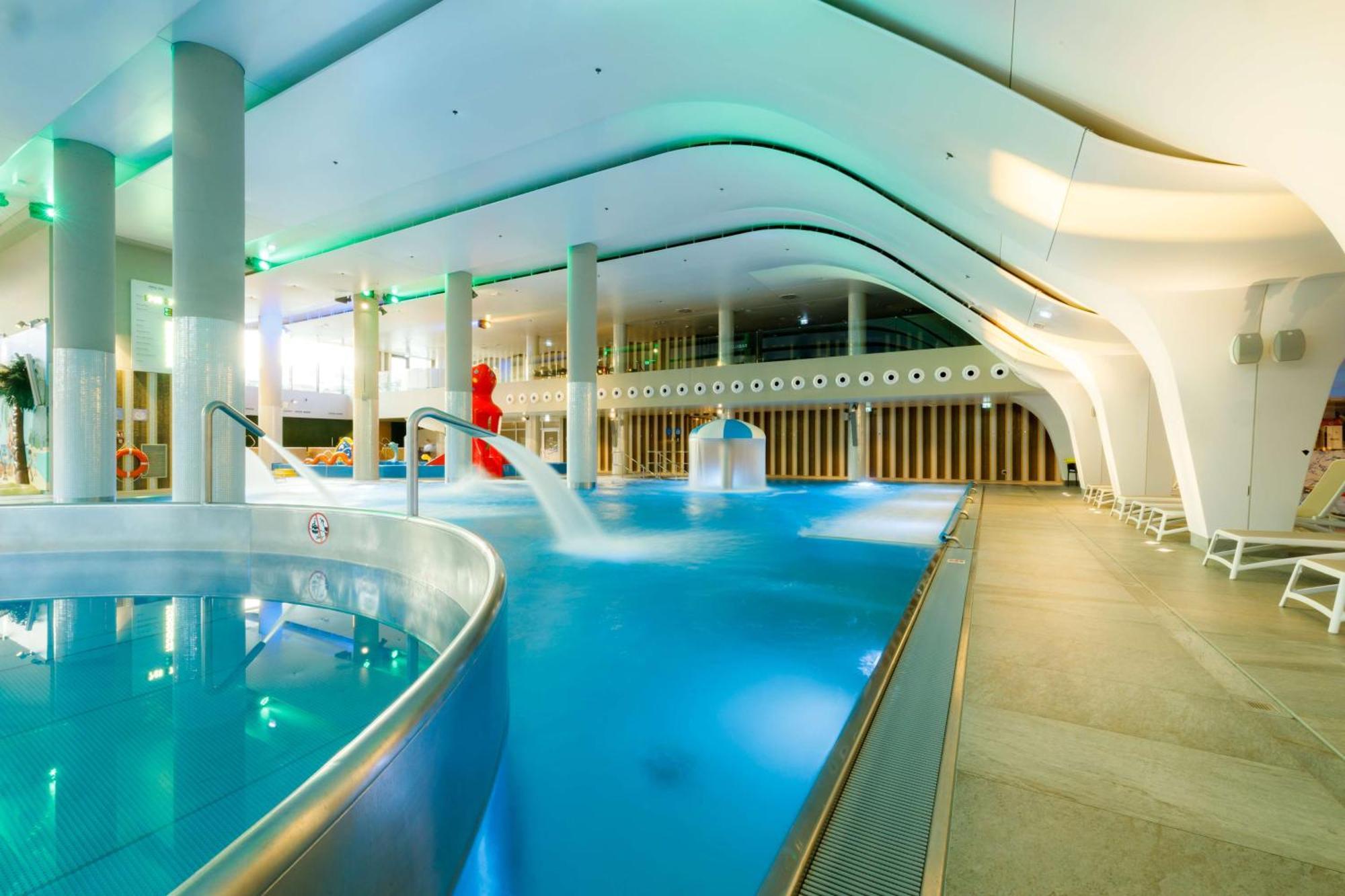Radisson Blu Resort Świnoujście Zewnętrze zdjęcie The photo shows a modern indoor swimming pool area with an elegant design. The pool features curved edges and is filled with clear, blue water. There are various amenities, such as jets for relaxation and possibly seating areas along the edges. The l