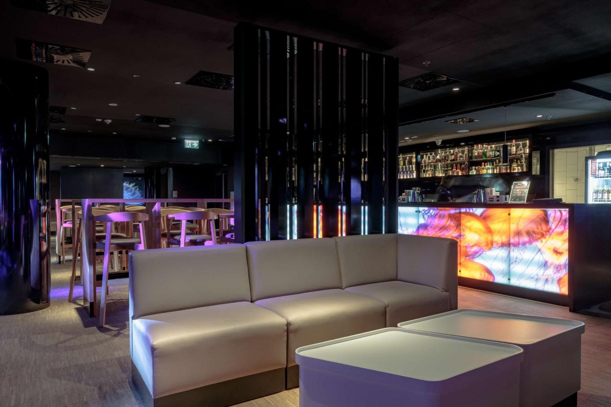 Radisson Blu Resort Świnoujście Zewnętrze zdjęcie The photo depicts a modern interior space, possibly a lounge or bar. There are sleek, minimalistic furniture pieces, including a large, curved sofa and contemporary coffee tables. The lighting is dim, with a blend of colorful ambient lights illuminat