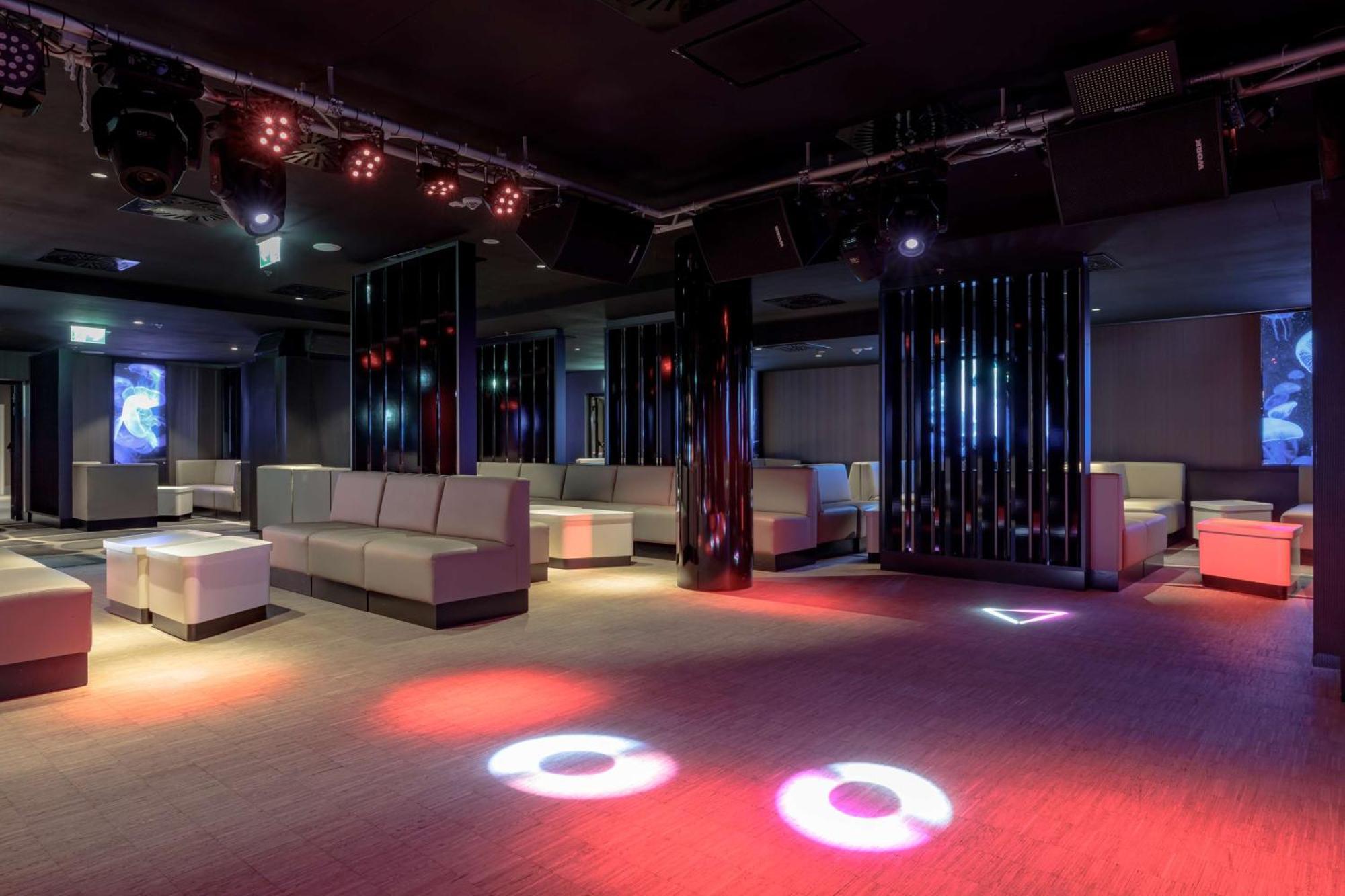 Radisson Blu Resort Świnoujście Zewnętrze zdjęcie The photo depicts a modern nightclub interior, featuring a spacious layout with sleek, minimalist seating arrangements. The room has plush seating along the walls, and the floor is illuminated with circular lights in varying colors, creating a vibran