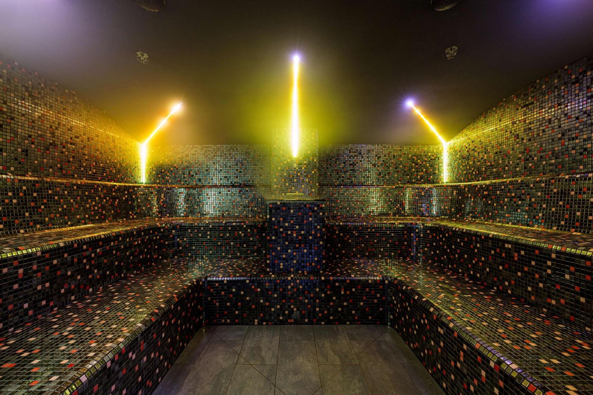 Radisson Blu Resort Świnoujście Zewnętrze zdjęcie The photo shows the interior of a steam room or sauna. The space is characterized by a series of benches that are built into the walls, allowing for multiple seating options. The walls are adorned with a mosaic of small, colorful tiles that create a 