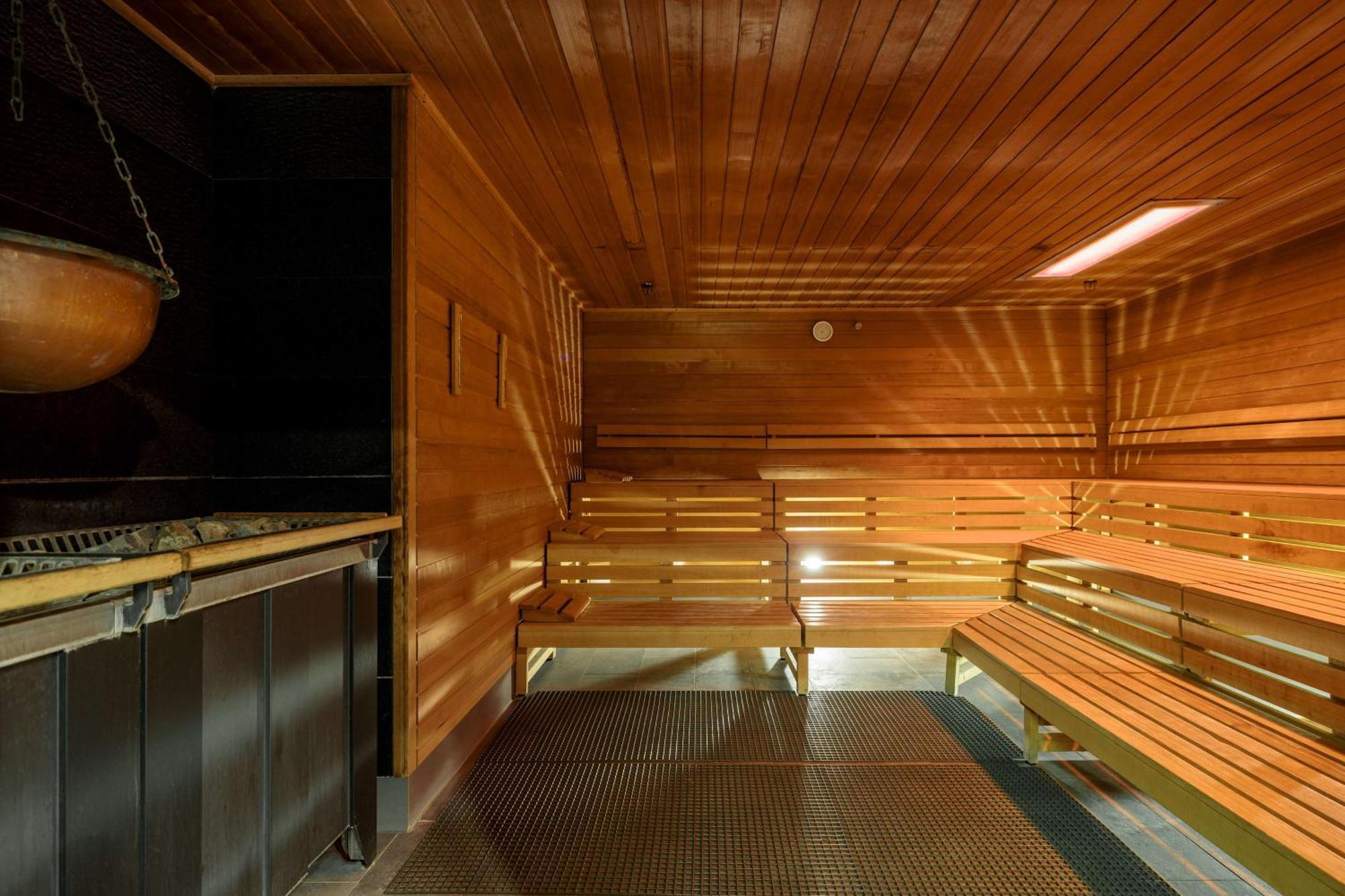 Radisson Blu Resort Świnoujście Zewnętrze zdjęcie The photo shows the interior of a sauna. The walls and benches are made of wood, creating a warm and inviting atmosphere. There is a heater, likely for generating steam, and a metal rack connected to it, perhaps for holding stones or water. The desig