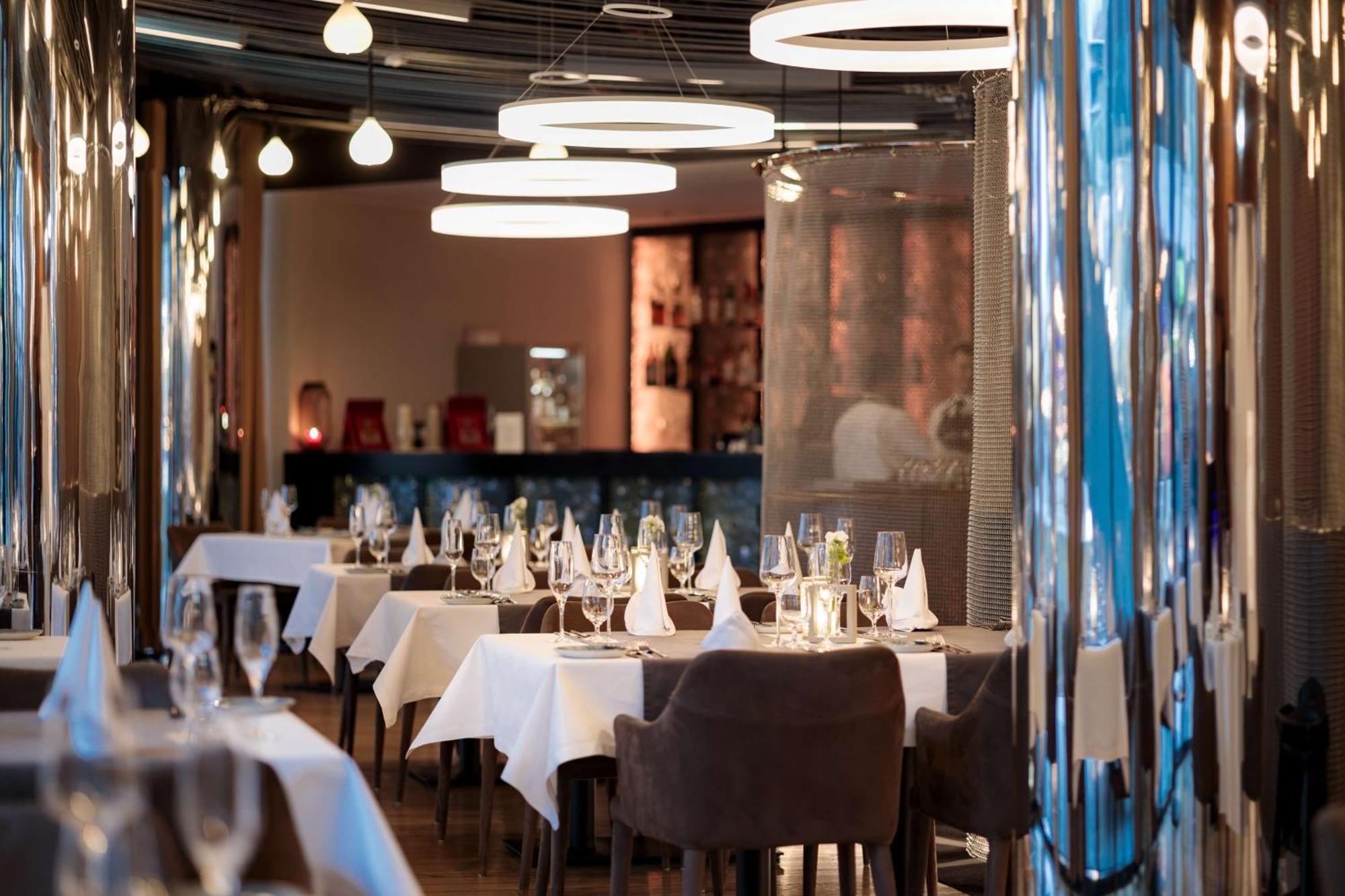 Radisson Blu Resort Świnoujście Zewnętrze zdjęcie The photo depicts an elegant restaurant interior. There are several tables covered with white tablecloths, each set with glassware and napkins, suggesting a fine dining experience. The chairs are upholstered, providing a comfortable seating arrangeme