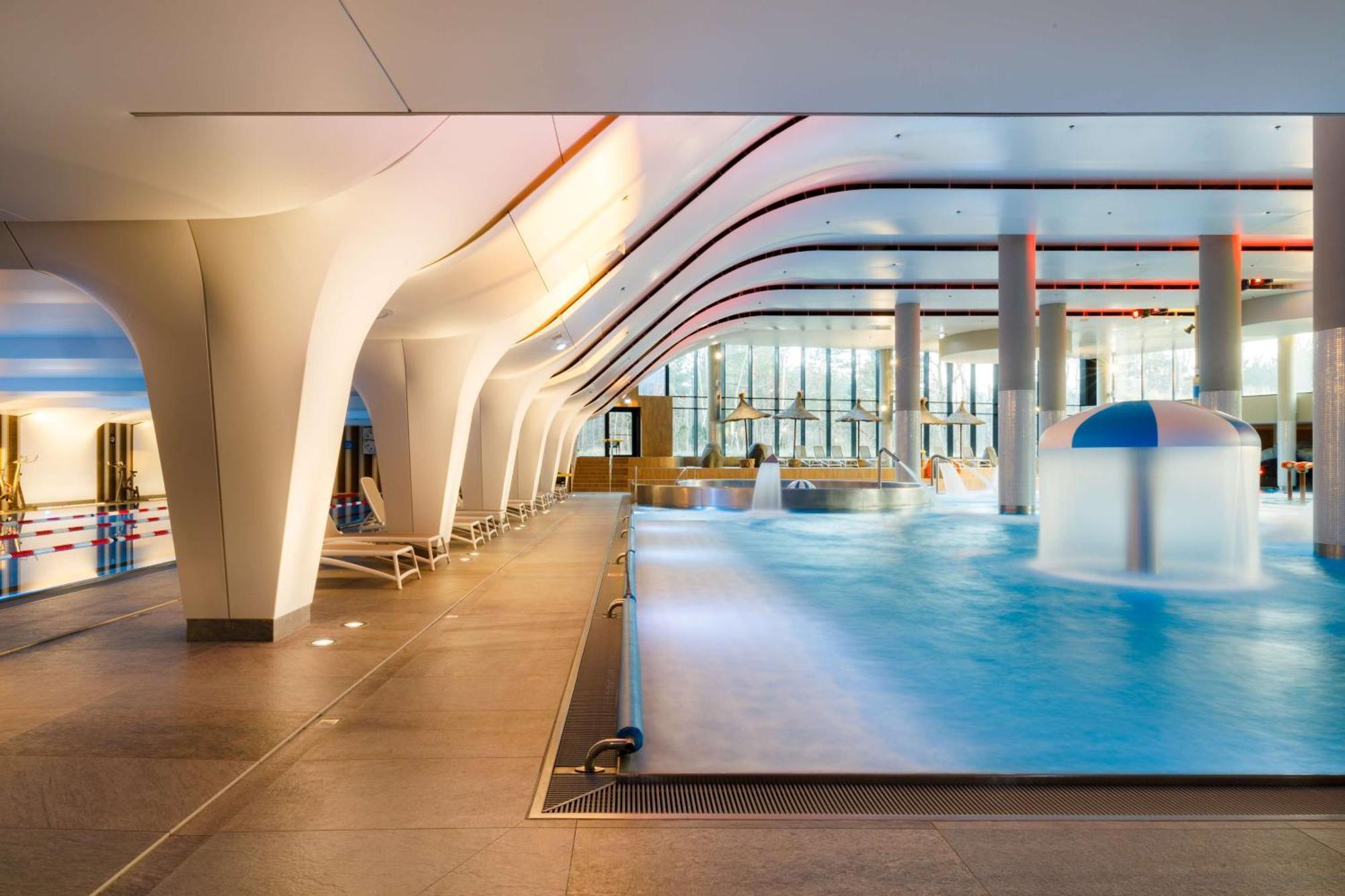 Radisson Blu Resort Świnoujście Zewnętrze zdjęcie The photo shows an indoor swimming pool area with a modern architectural design. The space features large windows allowing natural light to enter, and the interior has smooth, flowing lines in the ceiling and columns. The pool has a light blue water 
