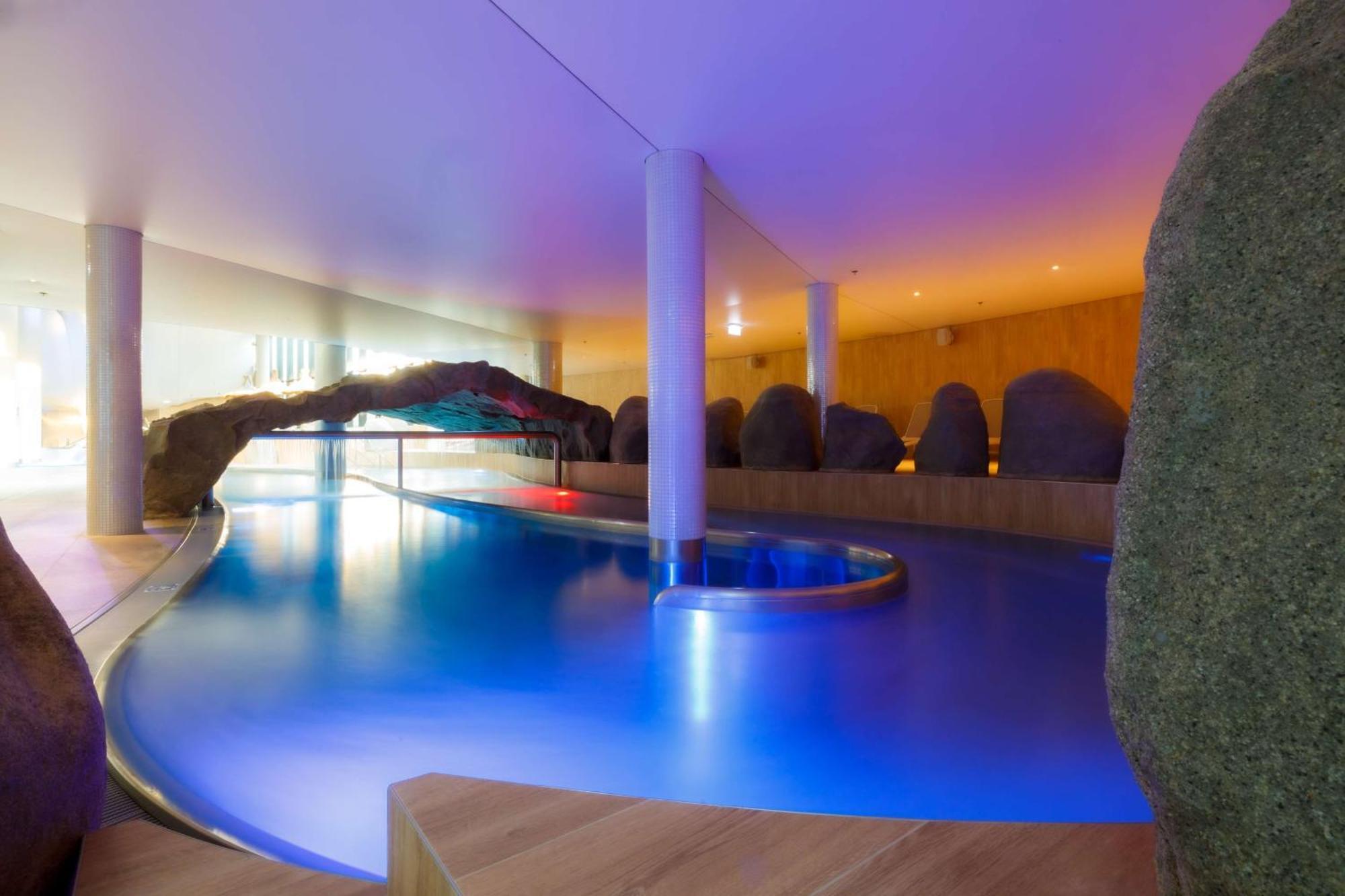 Radisson Blu Resort Świnoujście Zewnętrze zdjęcie The photo showcases an elegant indoor swimming pool area. The pool has a flowing, organic shape and is illuminated with soft blue and purple lighting, creating a calming ambiance. Surrounding the pool are smooth, natural-looking stones and wooden ele
