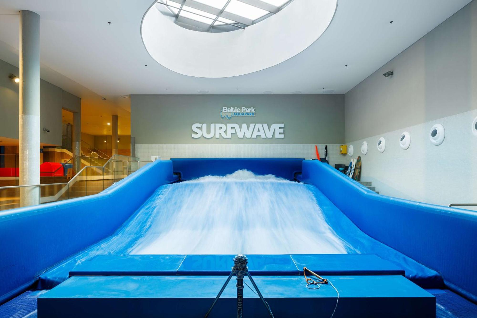 Radisson Blu Resort Świnoujście Zewnętrze zdjęcie The photo shows an indoor surfing attraction called "Surfwave." It features a large blue ramp with water flowing down it, creating a wave-like effect for surfing. Above the ramp, there is a sign that says "SURFWAVE." The area appears well-lit and mod